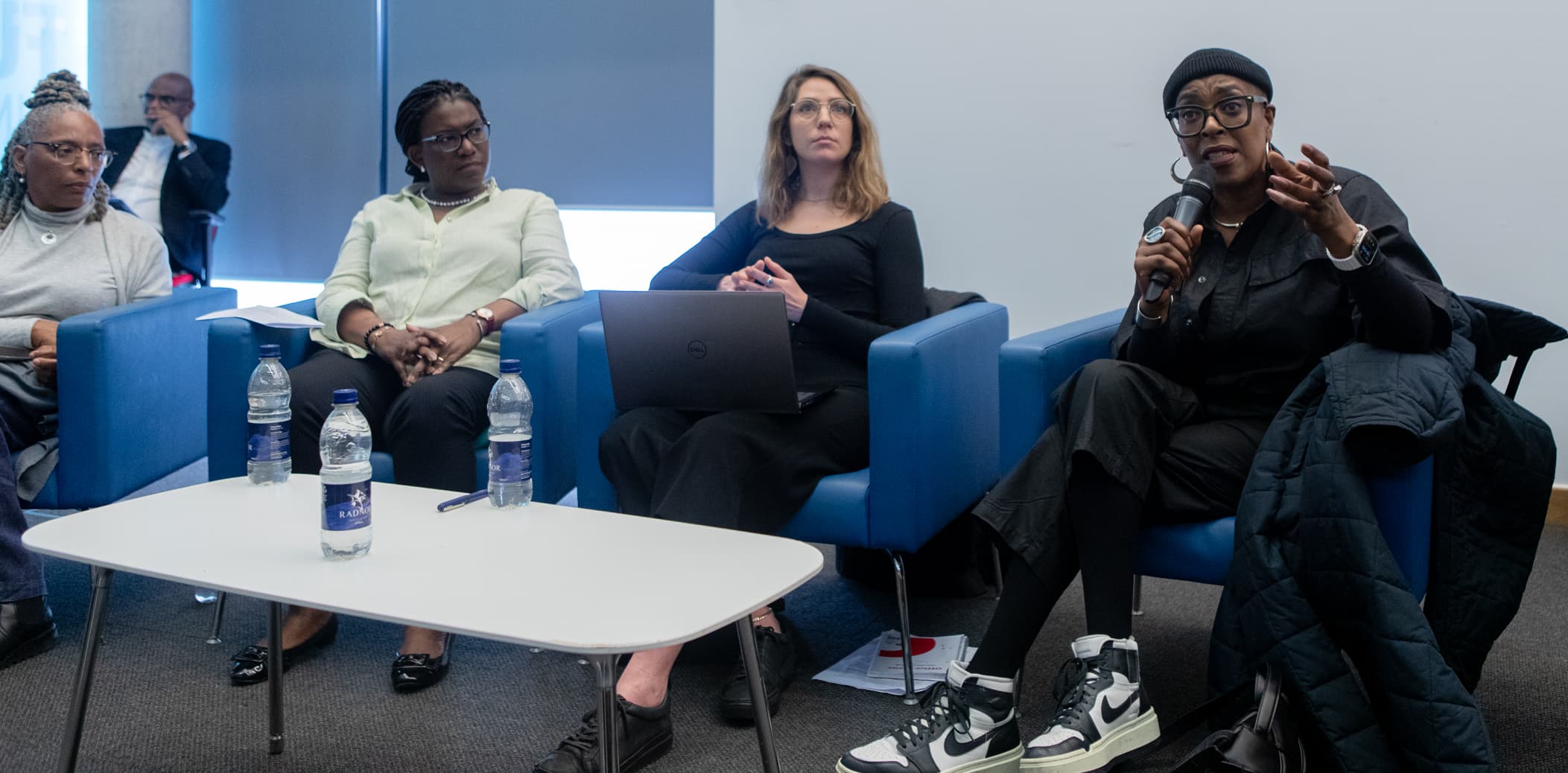 A panellist speaking into a microphone during a panel discussion at an APA conference, with fellow panellists seated beside her